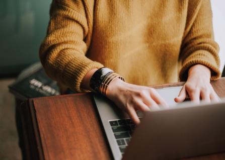 Torso photo of person in yellow sweater typing on a laptop